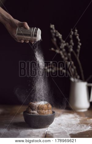 Detail of female hand sprinkling marble cake placed on a rustic wooden table with powdered sugar. Selective focus