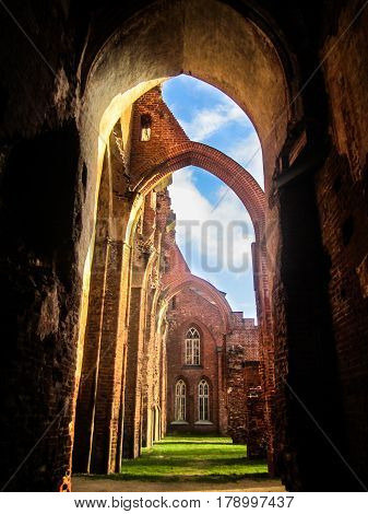 The ruins of the Gothic cathedral of red brick with blue sky and green grass