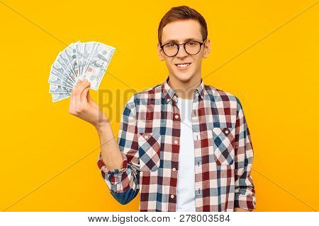 Happy Man In Glasses And A Plaid Shirt, With Dollar Bills, On Yellow Background