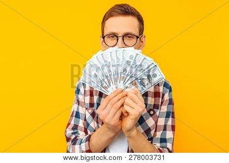 Happy Man In Glasses And A Plaid Shirt, With Dollar Bills, On Yellow Background