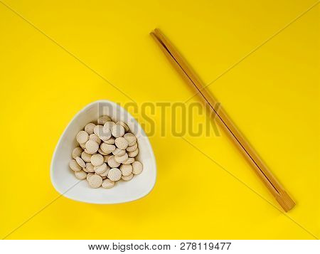 A Lot Of Pills In A White Bowl And Wooden Chopsticks On A Yellow Background. The Concept Of Overuse