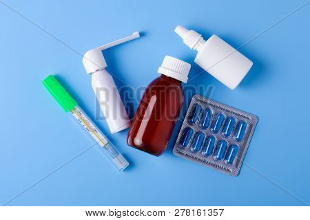 Blue Pills Capsules Nose Throat Spray Cough Syrup Thermometer Medicine Health On Blue Background Top