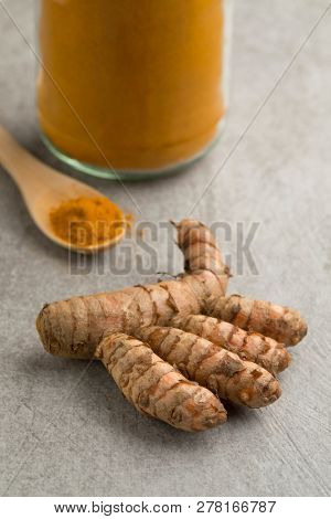 Fresh raw turmeric rhizome and powder in a jar and on a wooden spoon