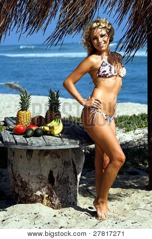 Ragazza bionda sexy del bikini in spiaggia in bikini rosa e marrone di Swimbay sotto un ombrello palapus w