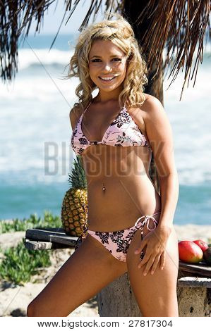 Ragazza bionda sexy del bikini in spiaggia in bikini rosa e marrone di Swimbay sotto un ombrello palapus w