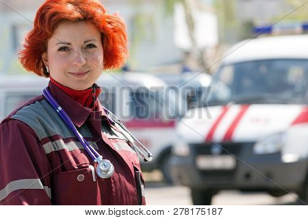 Happy Female Paramedic Standing At Ambulance Machines Background