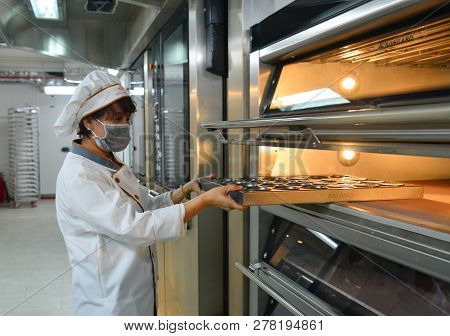 Saigon, Vietnam - Jan 9, 2019. Woman Cooking In The Kitchen, Puts Cakes In The Oven.