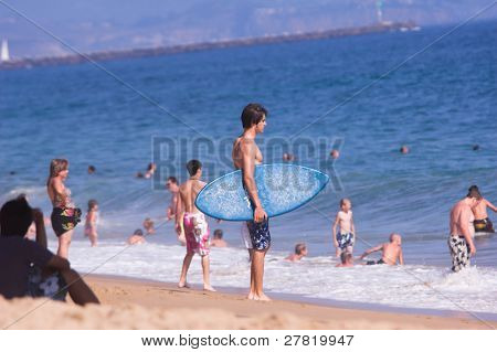 Mladý muž s skimboard hodnotí podmínky surfování na přeplněné pláži Balboa. Balboa Kalifornie