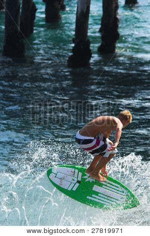 Mladý muž na zelené skimboard seškrtá proti ustupující příboj u Balboa Pier zároveň skimboard