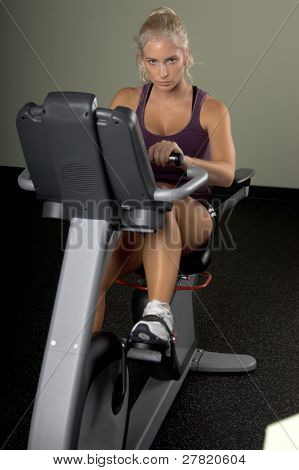 Krásná blonďatá žena během cardio cvičení na ležící rotoped v tělocvičně