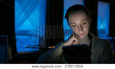 Woman Using Digital Tablet Computer Device In Cafe Of Cruise Ship. Evening Time, Lowlight. Technolog