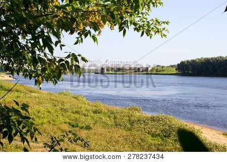 Wide Blue River. Ahead Of The Cathead Trees. The Leaves Are Green. Coast Overgrown With Green Grass.