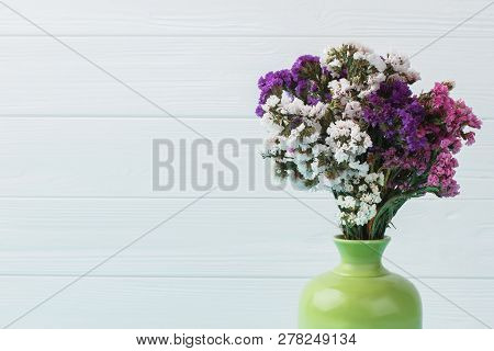 Different Statice Limonium Flowers In A Green Ceramic Vase. Close Up. Blue Wooden Background.