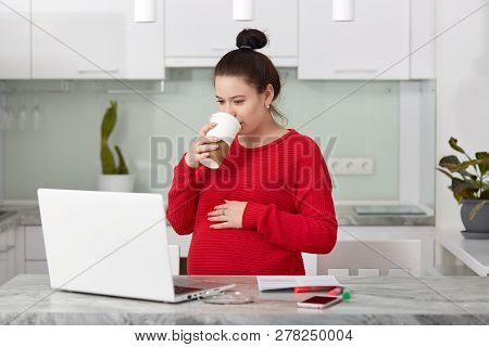 Busy Future Mother Focused At Laptop Compuer, Watches Training Webinar, Drinks Takeaway Coffee, Keep