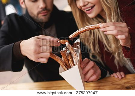 Close-up Of Young Couple Are Eating Churros At The Street Food Market.
