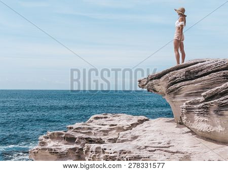 Female Enjoying The Balmy Sunshine Wearing Shorts, Crop Top And Sun Hat Standing On Sandstone Rocks 