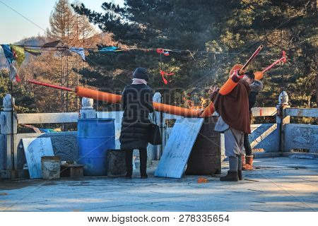 TUMEN, CHINA - DECEMBER 31, 2018: Three women parishioners set fire to the huge joss aroma incense sticks or candles in Hua-Yang temple in the Korean province of Jilin in The Yanbian Korean Prefecture