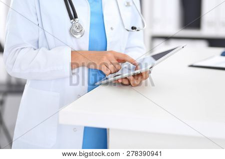 Close-up Of Female Physician Using Digital Tablet  While Standing Near Reception Desk At Clinic Or E