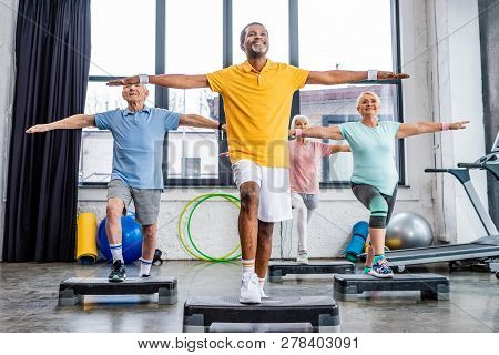 Smiling Senior Multicultural Athletes Synchronous Exercising On Step Platforms At Gym