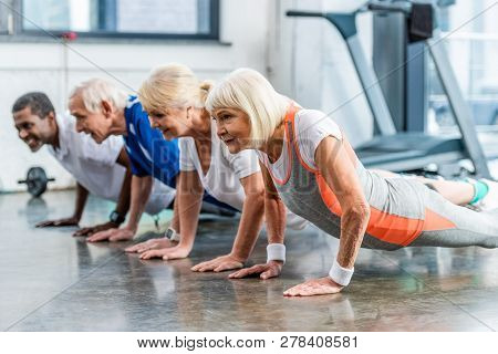 Happy Mutiethnic Senior Athletes Doing Plank At Sports Hall