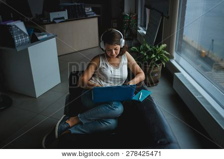 Young Woman Listening Music In Headphones And Working On Laptop On The Sofa In Office. Recreation, C