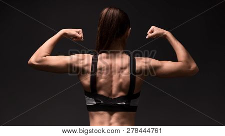 Fitness Girl Showing Bicepses And Back Muscles On A Dark Background.