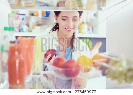 Portrait of female standing near open fridge full of healthy food, vegetables and fruits. Portrait of female