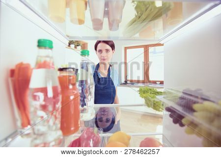 Portrait of female standing near open fridge full of healthy food, vegetables and fruits. Portrait of female