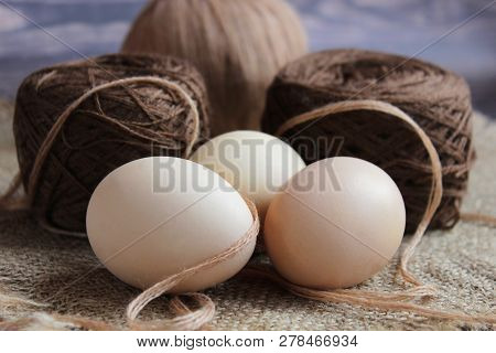 Close-up Of Three Fresh Eggs And Thread. On The Background Of A Ball Of Yarn For Knitting Light Beig