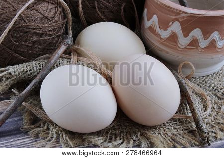 Composition Of Three Eggs, Wooden Sticks And Mugs Of Clay On A Beige Background