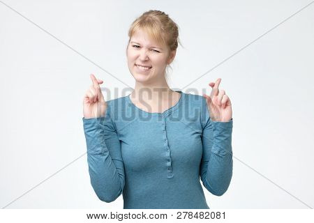 Glad Happy Blonde Woman Wears Blue Shirt, Smiles Broadly, Keeps Fingers Crossed, Hopes For Good Luc