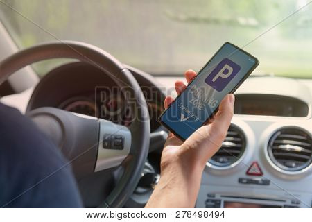 Driver using smartphone app to pay for parking in the paid parking zone in a city