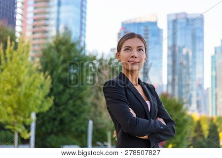 Asian businesswoman. Happy business woman portrait pensive looking up contemplative of her career. City job employment. Chinese professional in black suit confident with crossed arms.
