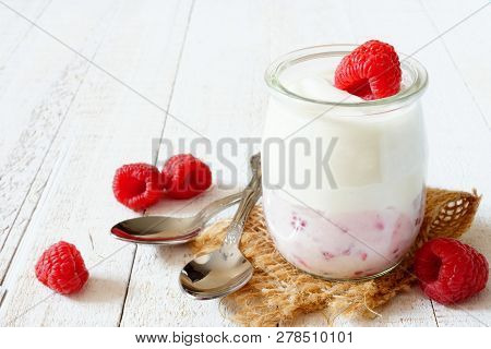 Jar Of Yogurt With Raspberry Fruit On The Bottom. Side View On A White Wood Background.