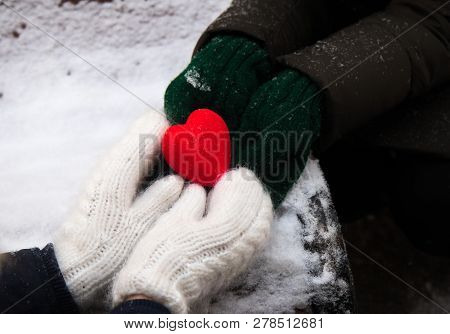 Hands In White And Green Mitterns With Red Heart On The Snow