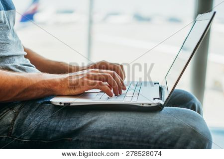 Young Man Using Laptop In Airport Terminal
