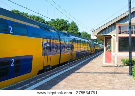 Dutch railway station with yellow train in little village Den Dolder