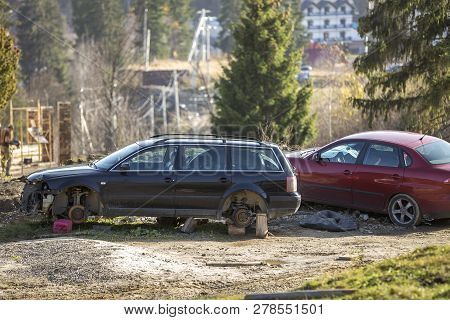 Red Car Parked In Recreation Zone And Old Rusty Broken Trash Car After Crash Accident Without Wheels