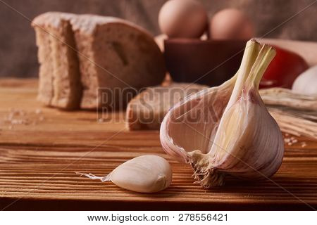Garlic On A Wooden Table With Eggs In Clay Bowl, Tomato, Battledore And Wheat Sprouts