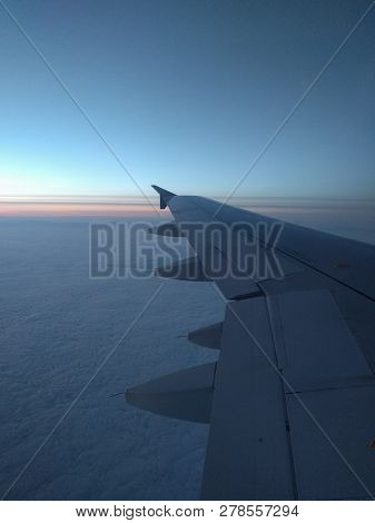 View From Airplane Window To Beautiful Sunrise Or Sunset. Wing Of Plane And Clouds In The Sky.