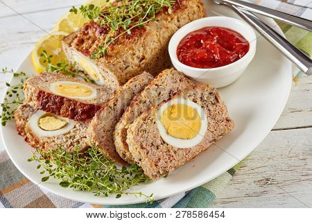 Meatloaf Stuffed With Hard-boiled Egg Served With Tomato Sauce And  Lemon Slices On A White Plate On