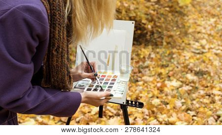 Close-up Of Young Girl Artist That Paints A Picture On The Easel In The Autumn Park