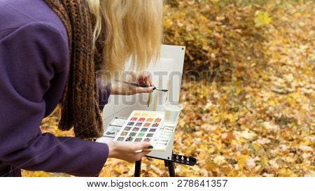Close-up Of Young Girl Artist That Paints A Picture On The Easel In The Autumn Park