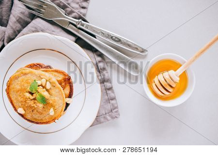 Flat Lay Banana Pancakes With Walnuts And Cedar Nuts, Honey And Mint, Honey Dipper On A White Backgr