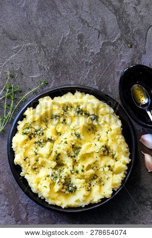 Potato mash with olive oil, garlic, lemon, and herbs.  Top view on dark slate, in black dish.