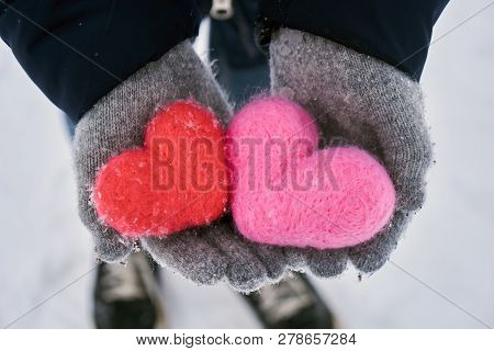 Hands In Wollen Gloves Holding Two Woolen Hearts Covered With Snowflakes