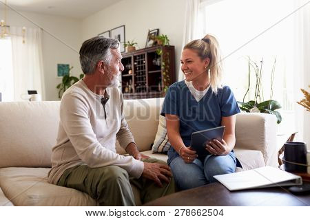 Female healthcare worker using a tablet computer with a senior Hispanic man during a home visit