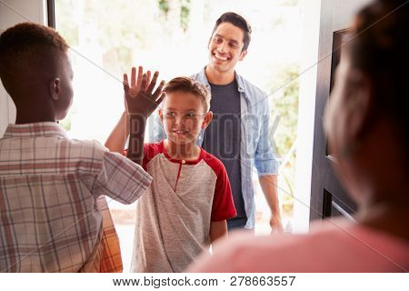The two pre-teen boys high five in the open doorway, as dad drops his son off at his friendsÃ house