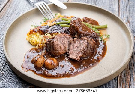 Traditional German braised pork cheeks in brown sauce with Swiss rÃ¶sti and green beans as closeup on a modern design plate 
