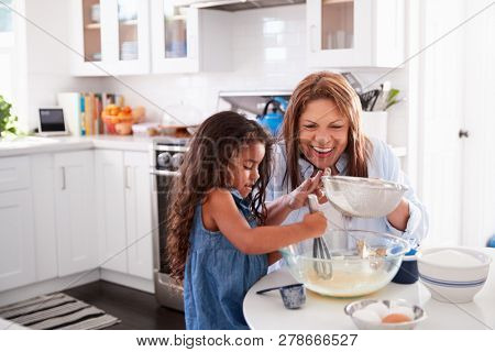Young Hispanic girl making cake in the kitchen with her grandma, looking down